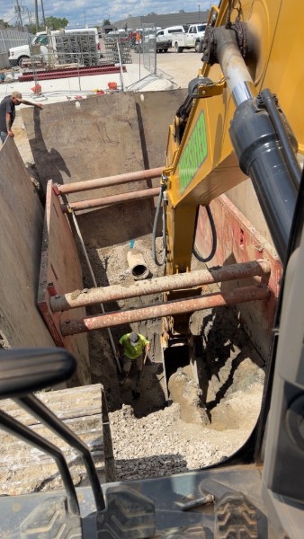 Excavator attachment working over a shored trench