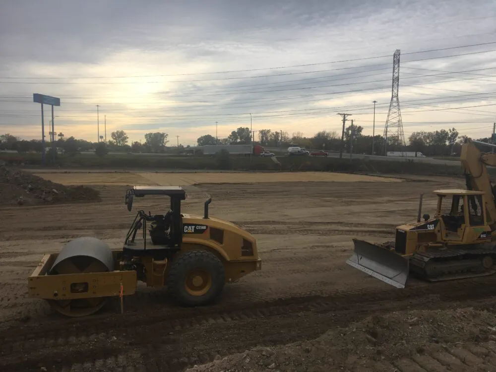 Roller and dozer compacting a graded pad